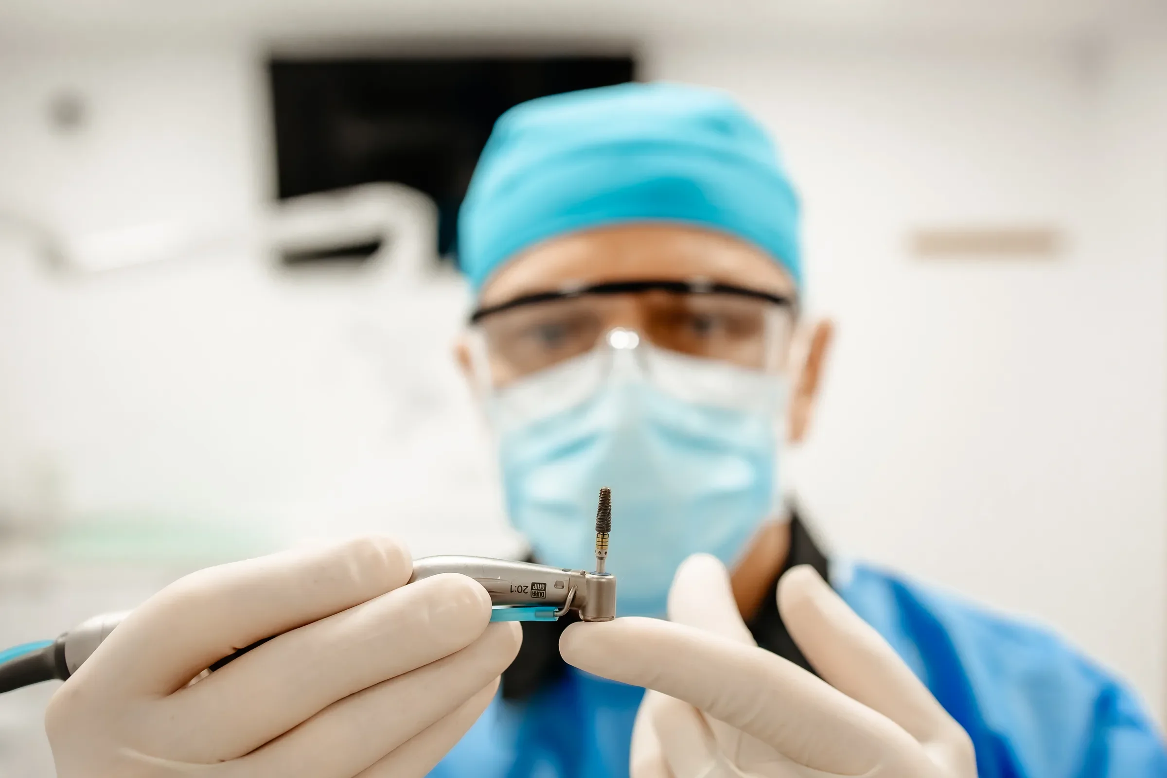 Mâini în mănuși care țin un implant dentar pe instrumentul de inserare